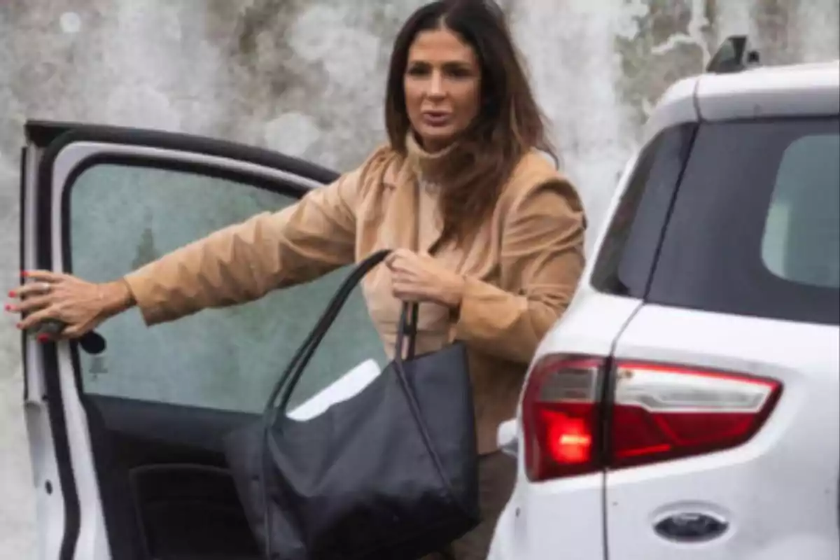 Woman in a beige coat getting out of a white car while holding a black bag