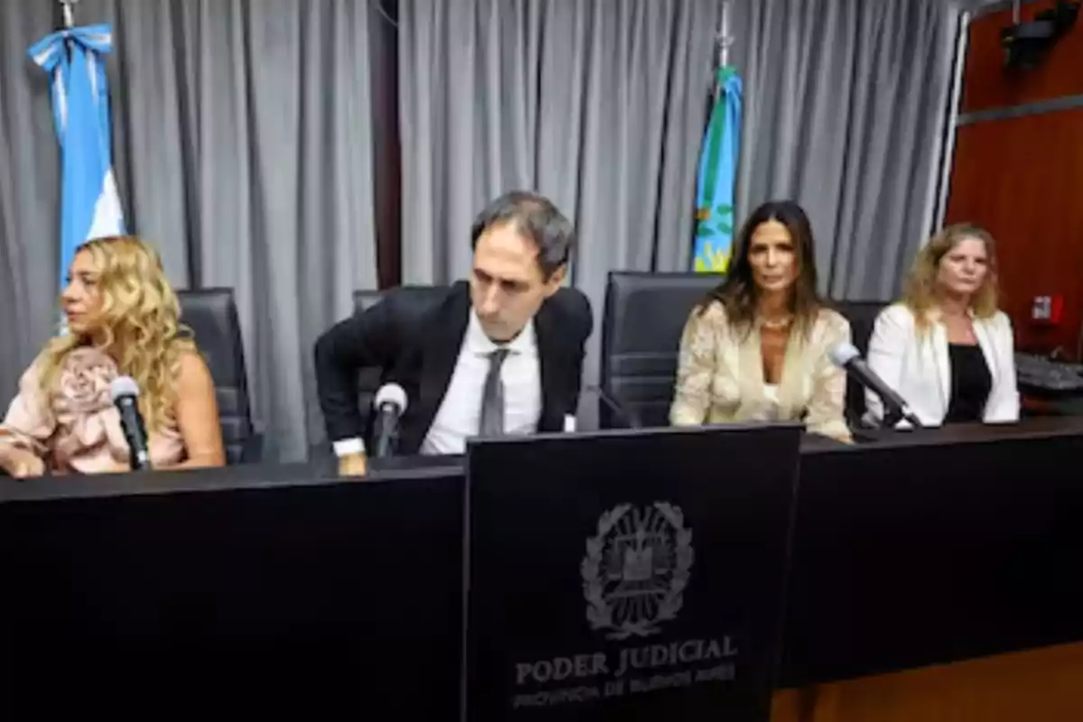 Four people seated at a table of the Judiciary of the Province of Buenos Aires with Argentine flags and microphones in front of them Four people seated at a table of the Judiciary of the Province of Buenos Aires with Argentine flags and microphones in front of them