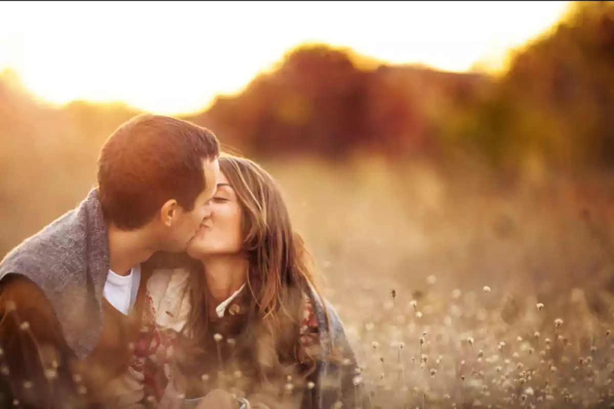 Couple kissing in a field at sunset with warm light and a romantic atmosphere Couple kissing in a field at sunset with warm light and a romantic atmosphere