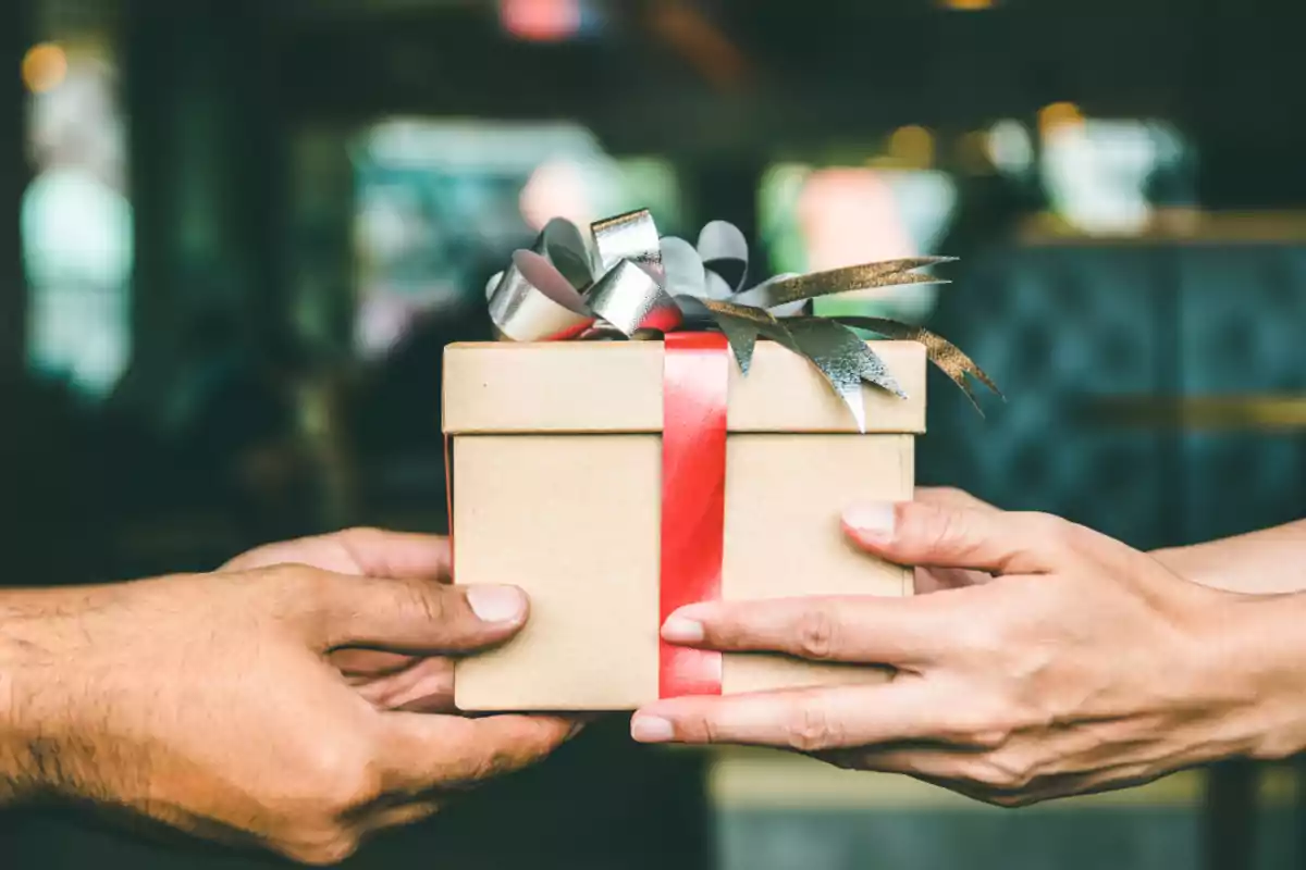 Dos personas intercambian una caja de regalo envuelta con un lazo rojo y plateado Dos personas intercambian una caja de regalo envuelta con un lazo rojo y plateado