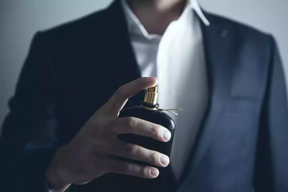 Man in a suit holding a black and gold perfume bottle Man in a suit holding a black and gold perfume bottle