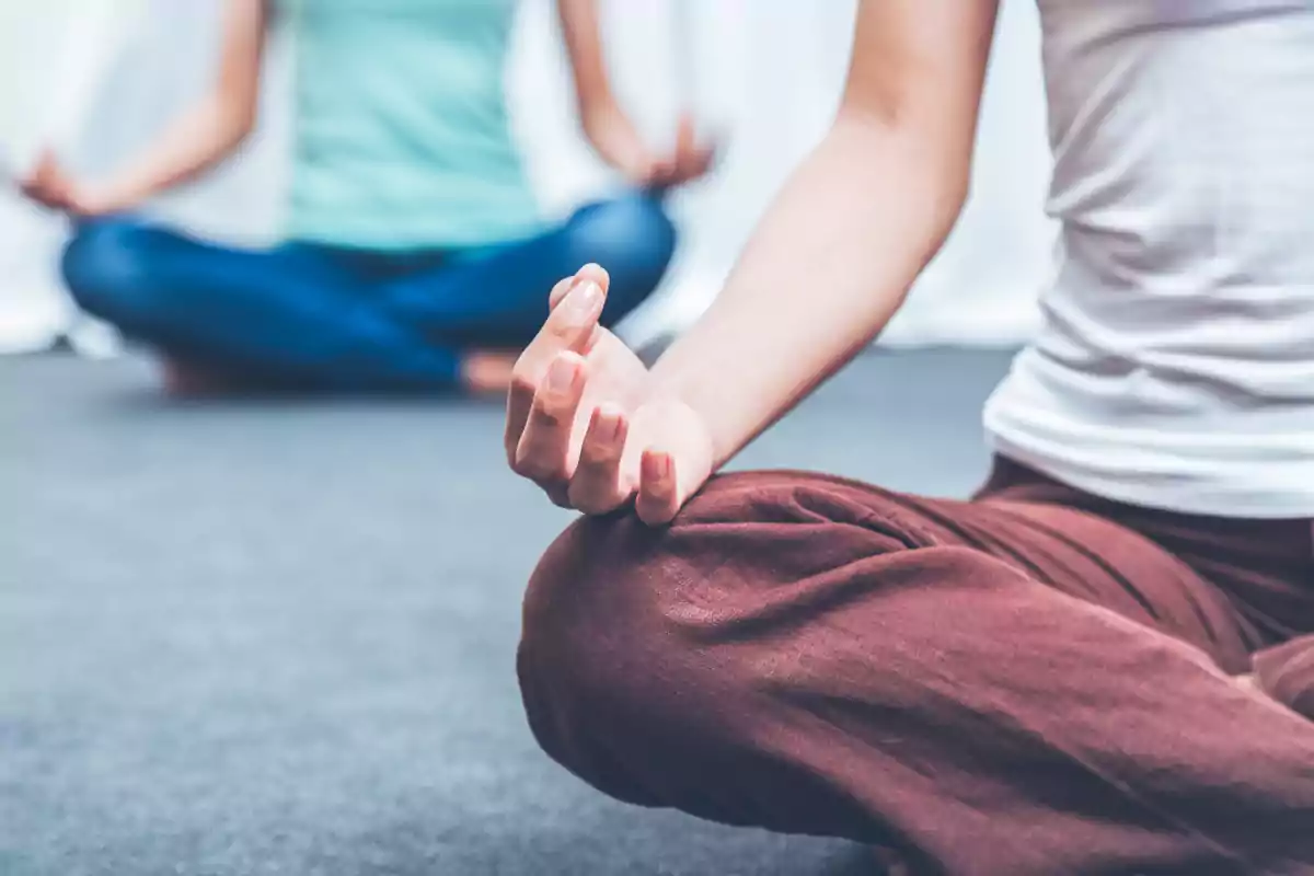 Two people sitting on the floor practicing meditation with their legs crossed and their hands resting on their knees Two people sitting on the floor practicing meditation with their legs crossed and their hands resting on their knees