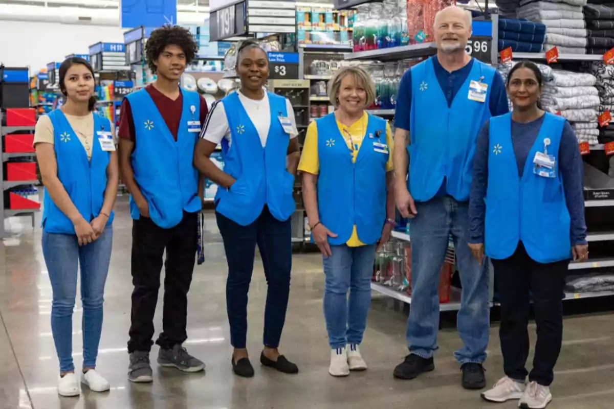 Un grupo de empleados de una tienda, vestidos con chalecos azules, posan juntos en un pasillo lleno de productos.