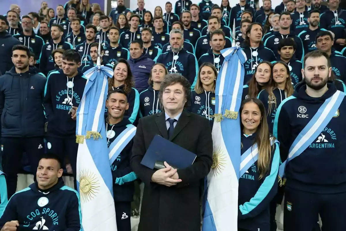 Un grupo de personas vestidas con ropa deportiva de Argentina posando para una foto, con dos banderas argentinas y una persona en el centro sosteniendo un documento.