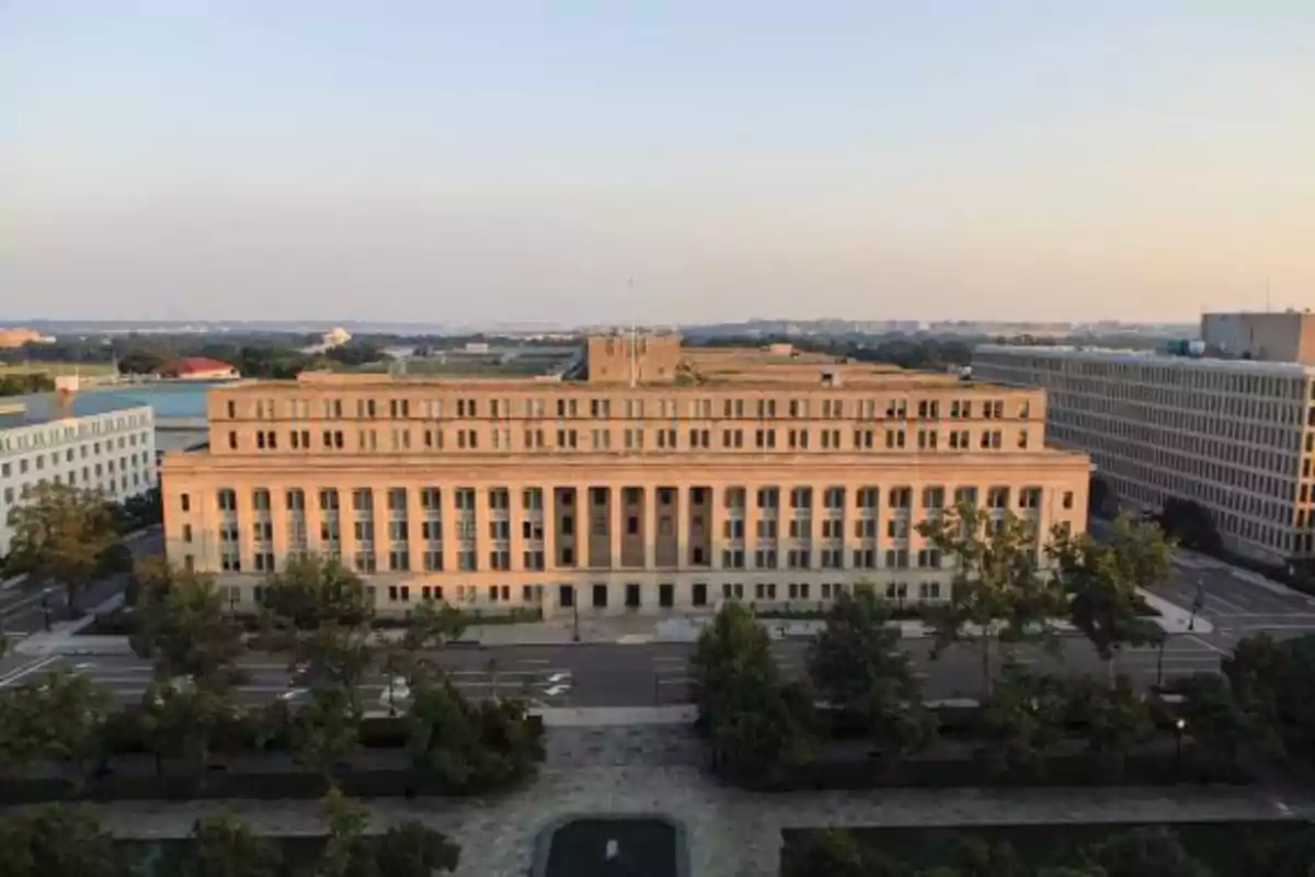 Edificio gubernamental de estilo clásico rodeado de árboles y calles en una ciudad al atardecer.