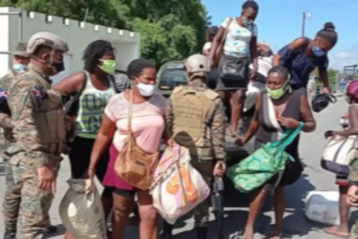 Un grupo de mujeres con mascarillas y bolsas desciende de un vehículo militar mientras varios soldados las observan en una calle al aire libre