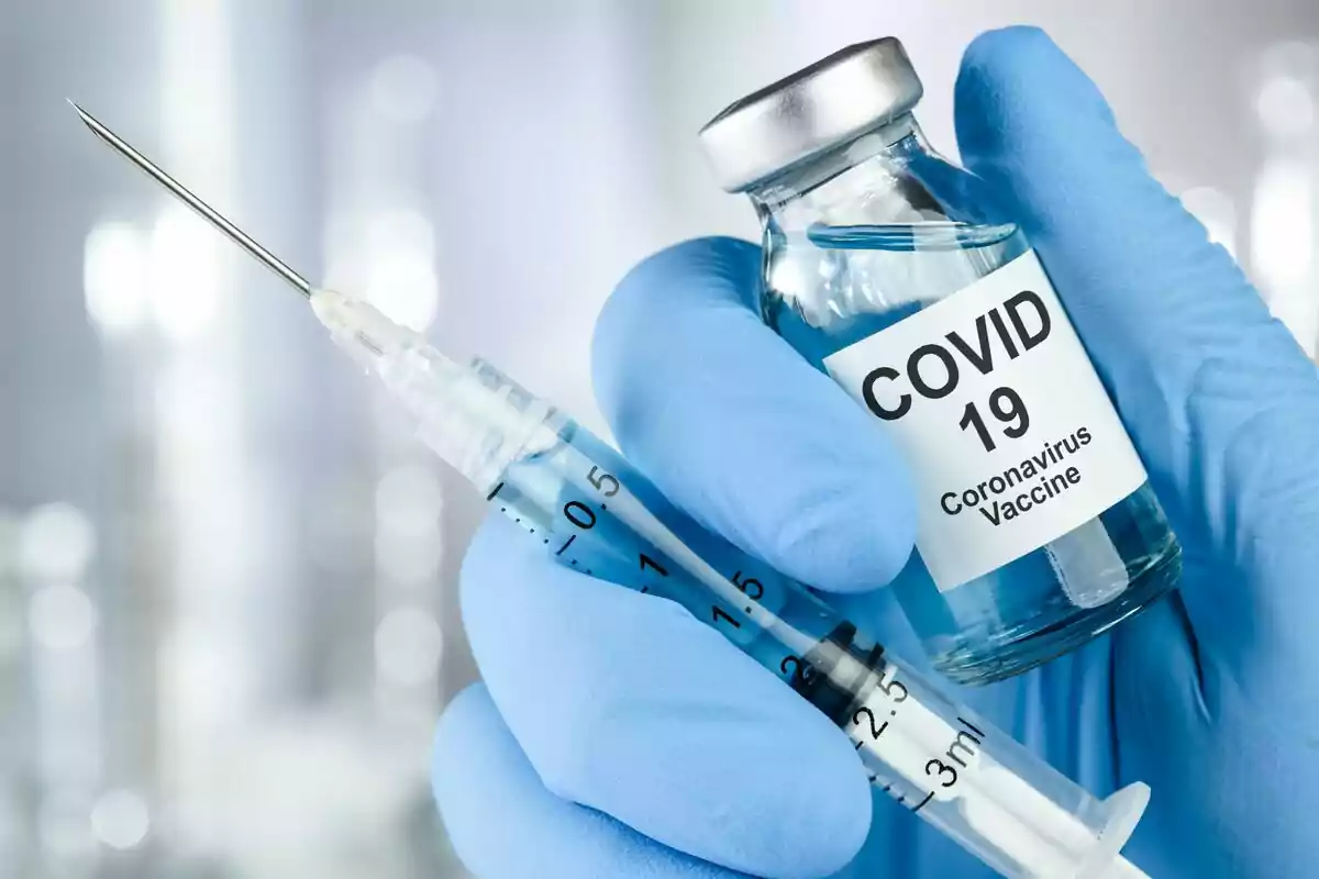Hand with blue glove holding a syringe and a vial of COVID-19 vaccine. Hand with blue glove holding a syringe and a vial of COVID-19 vaccine.