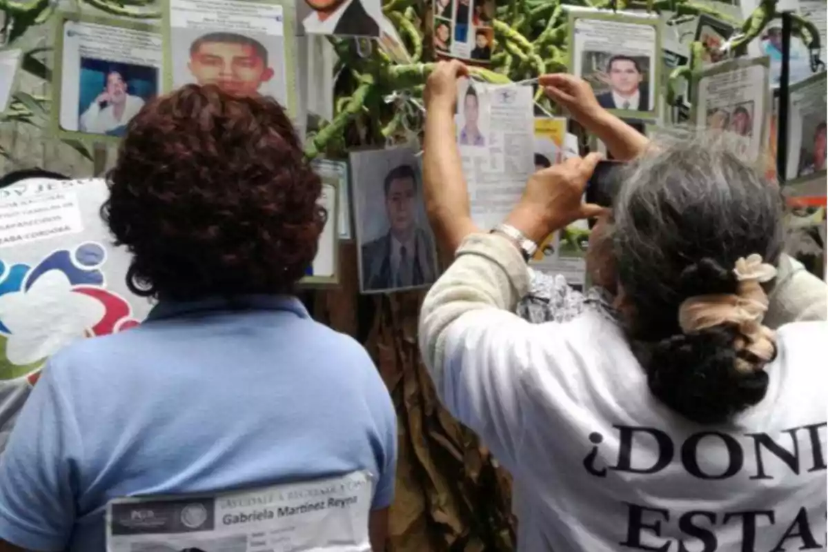 Two people observe and photograph posters of missing persons hanging on a wall.