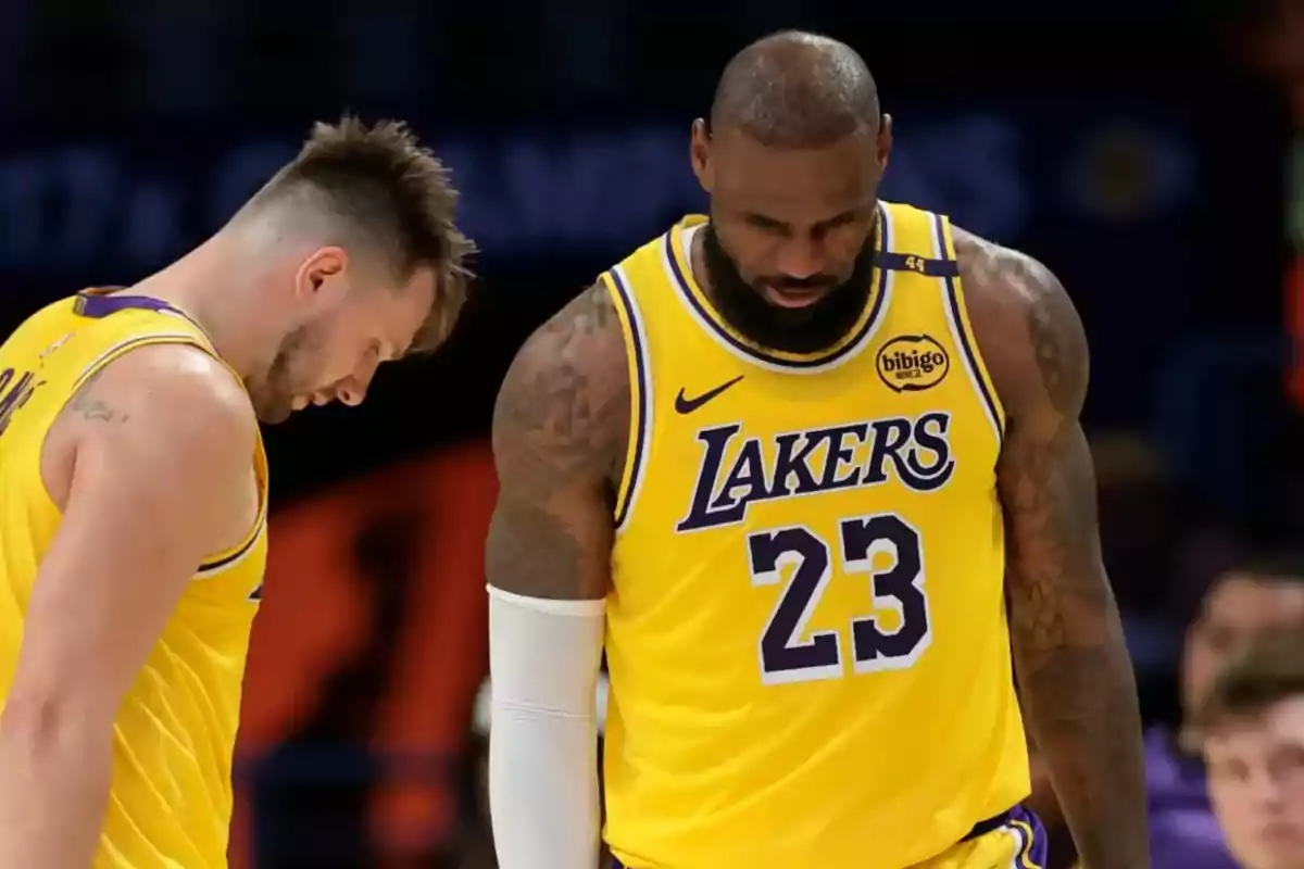Two basketball players in yellow Lakers uniforms, one of them with the number 23, are looking down at the court.