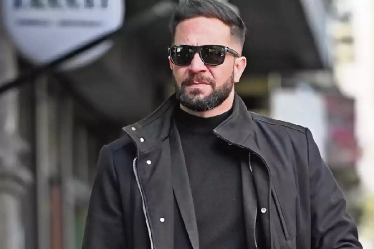 Hombre con barba y gafas de sol vistiendo ropa negra caminando por la ciudad