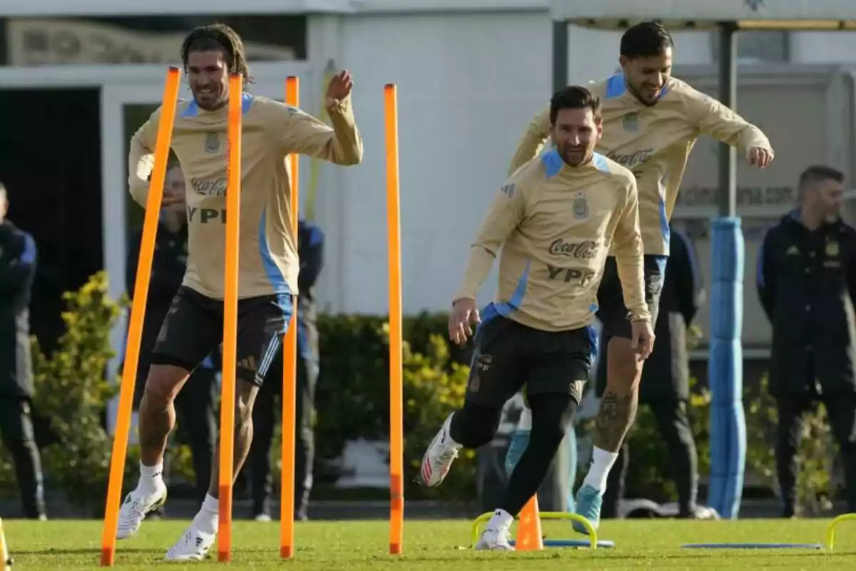 Jugadores de la selección argentina de fútbol entrenando y sonriendo mientras realizan ejercicios de agilidad en el campo