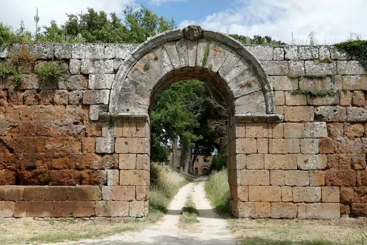 Un antiguo arco de piedra en un camino rodeado de vegetación y un cielo parcialmente nublado. Un antiguo arco de piedra en un camino rodeado de vegetación y un cielo parcialmente nublado.