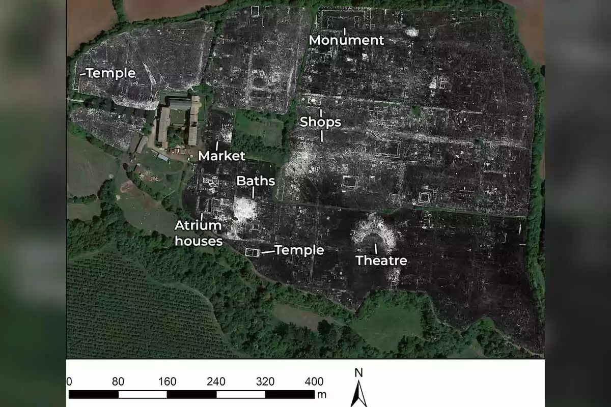 Imagen aérea de un sitio arqueológico que muestra la disposición de estructuras antiguas como templos, un teatro, un mercado, baños, casas con atrio, tiendas y un monumento, con un mapa de escala en la parte inferior. Imagen aérea de un sitio arqueológico que muestra la disposición de estructuras antiguas como templos, un teatro, un mercado, baños, casas con atrio, tiendas y un monumento, con un mapa de escala en la parte inferior.