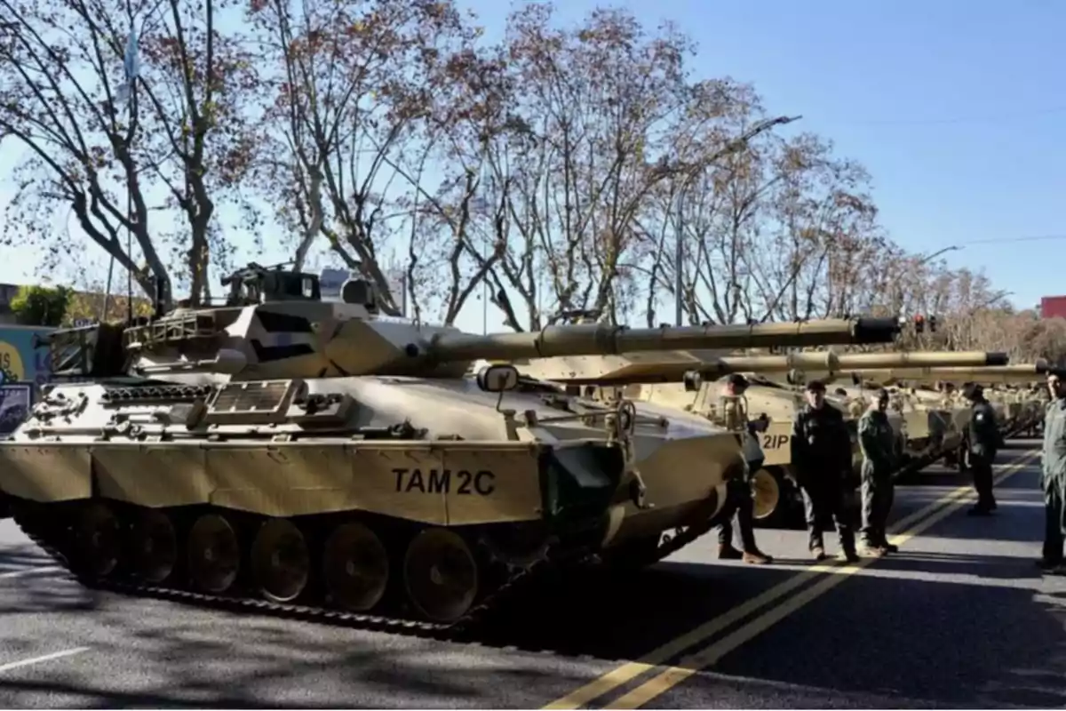 Tanques militares TAM 2C alineados en una calle con soldados de pie a su lado y árboles al fondo.