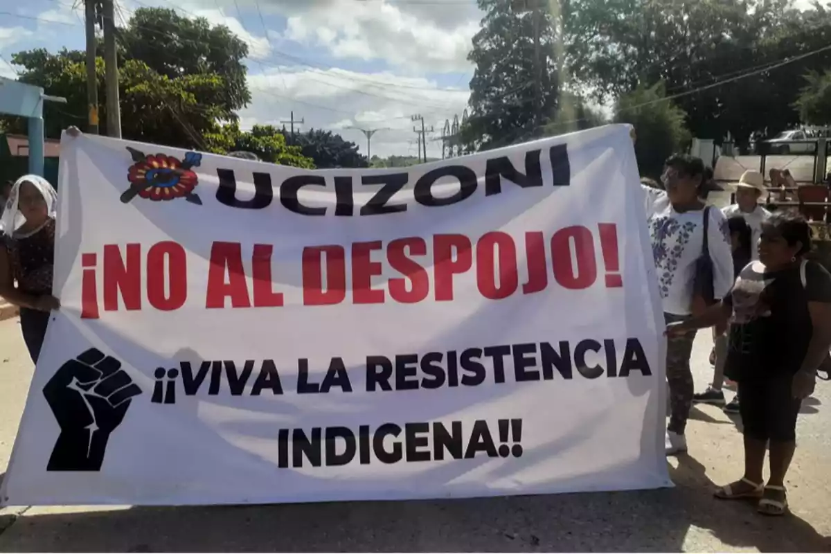 People hold a white blanket with large letters that reads UCIZONI No to dispossession! Long live indigenous resistance! during a street protest under the sunlight. People hold a white blanket with large letters that reads UCIZONI No to dispossession! Long live indigenous resistance! during a street protest under the sunlight.