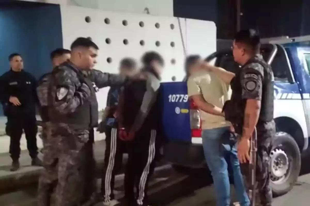 Varios policías detienen a tres personas junto a una patrulla durante la noche