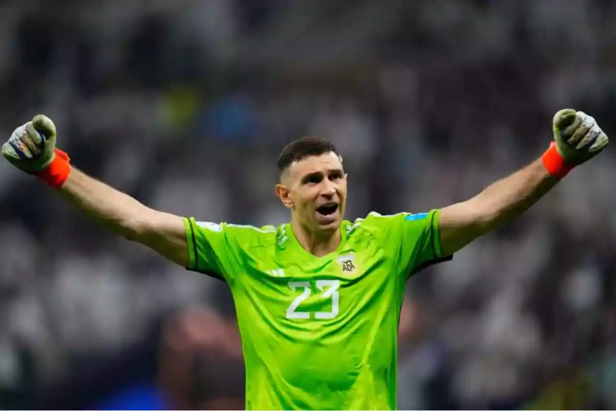 Un jugador de fútbol con uniforme verde levanta los brazos en señal de celebración.