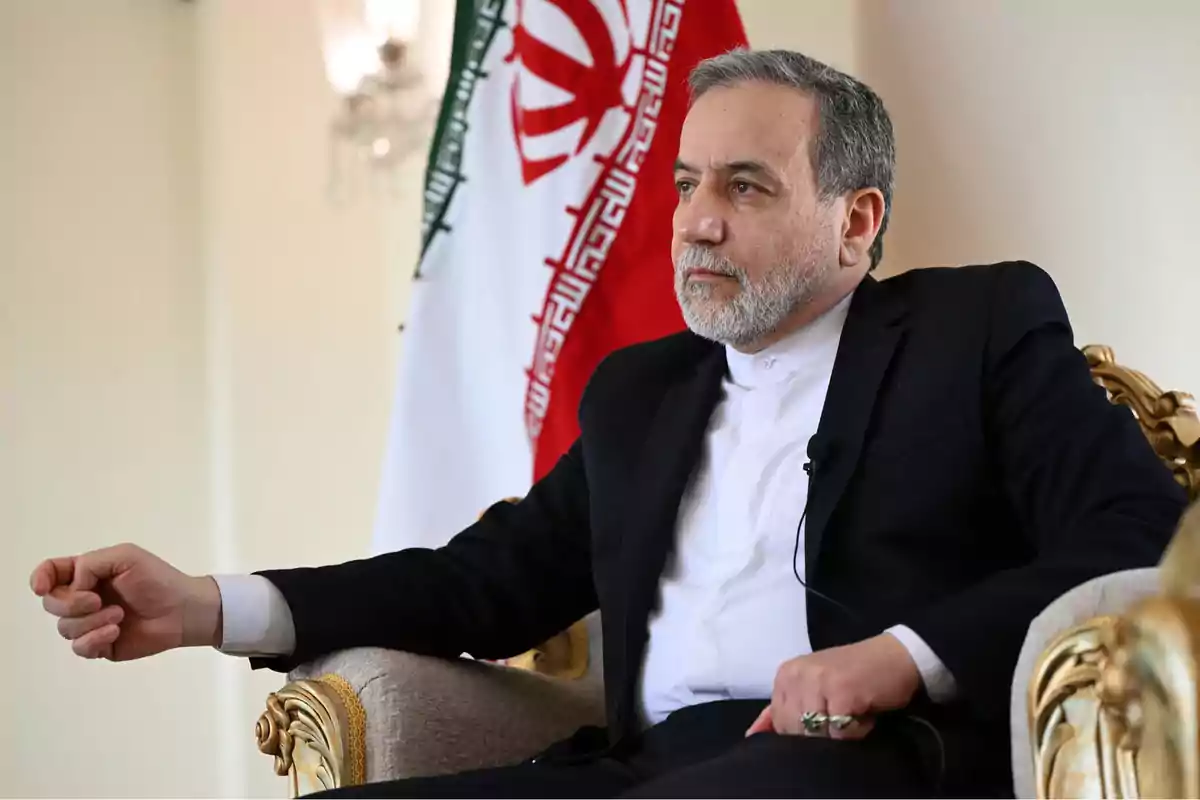 Hombre de mediana edad con barba sentado en un sillón elegante con una bandera de Irán al fondo Hombre de mediana edad con barba sentado en un sillón elegante con una bandera de Irán al fondo
