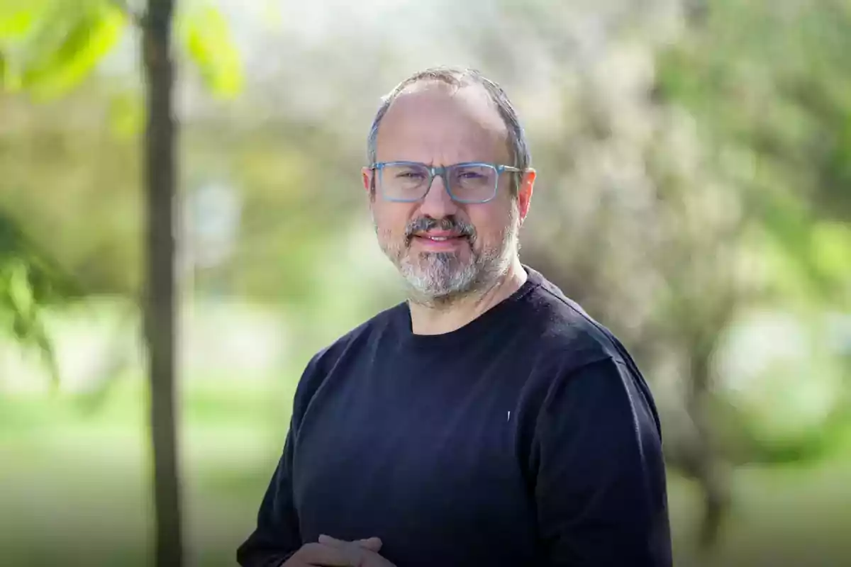 Middle-aged man with glasses and a beard posing outdoors with a background of trees and blurred vegetation Middle-aged man with glasses and a beard posing outdoors with a background of trees and blurred vegetation