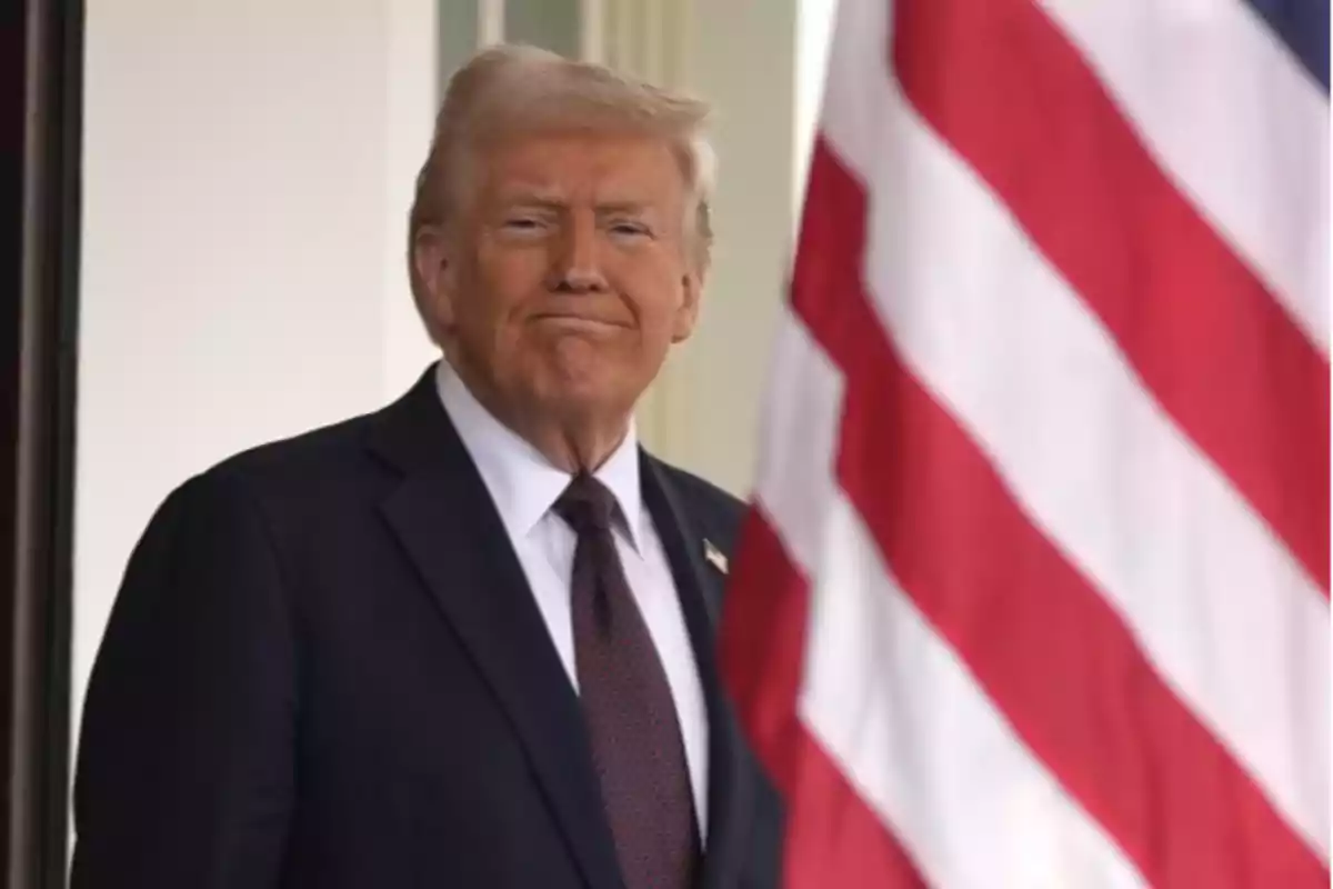 A man in a dark suit and tie is standing next to a United States flag.