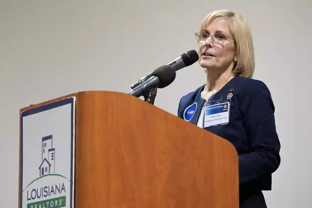 A person speaking at a podium with a microphone and a sign that says A person speaking at a podium with a microphone and a sign that says
