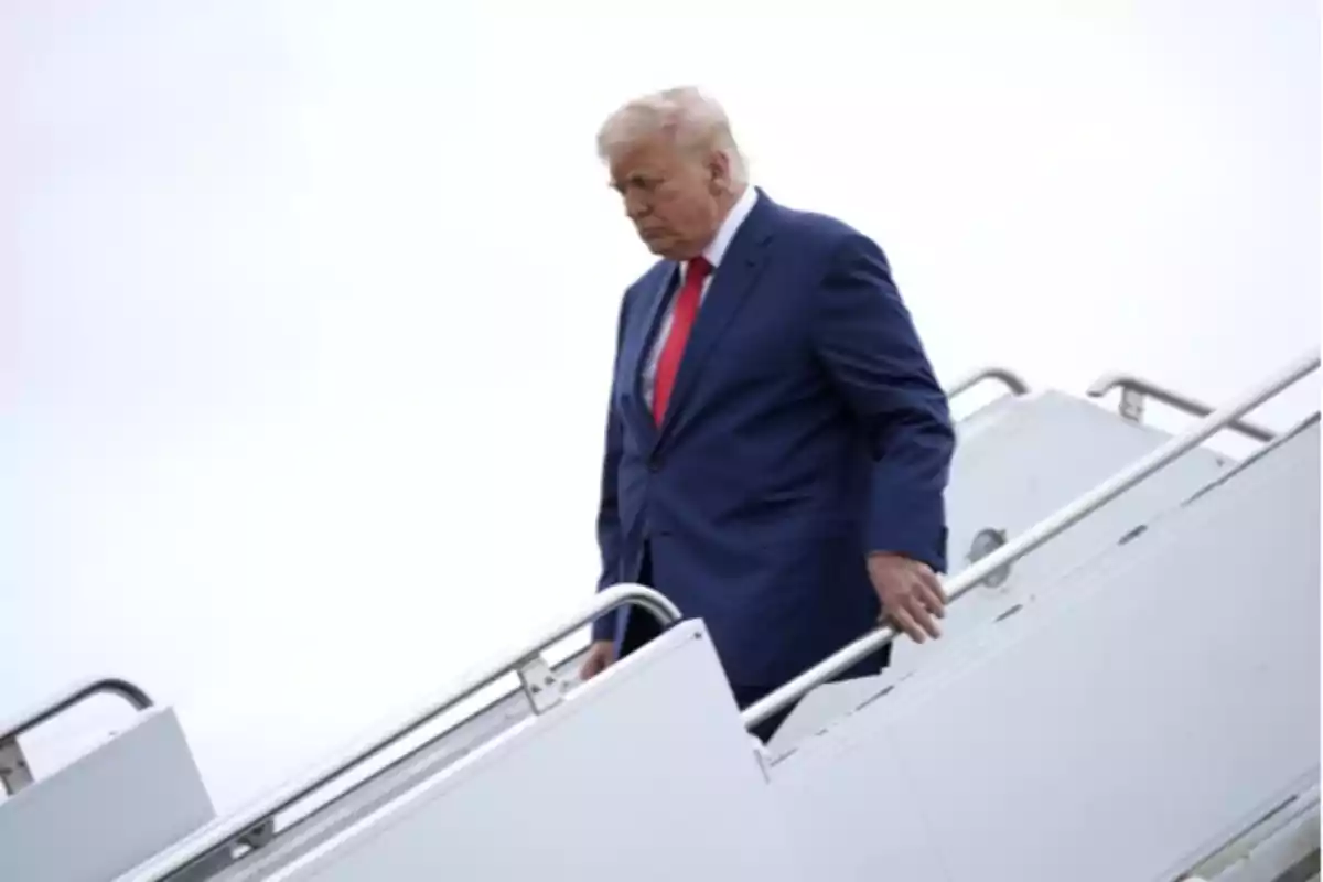 Hombre de cabello rubio con traje azul y corbata roja bajando por la escalera de un avión Hombre de cabello rubio con traje azul y corbata roja bajando por la escalera de un avión