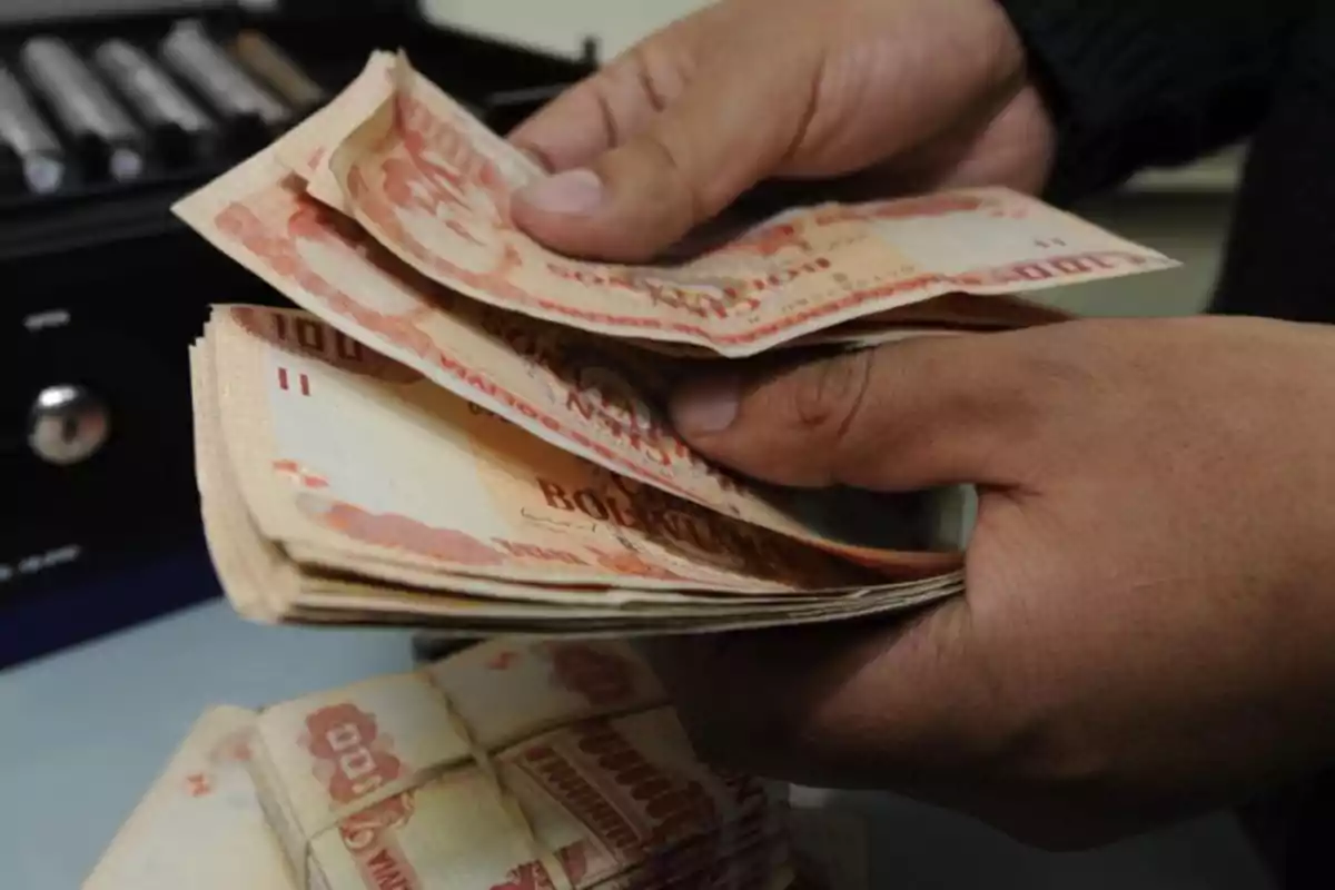 Una persona contando billetes de bolivianos con una máquina contadora en el fondo. Una persona contando billetes de bolivianos con una máquina contadora en el fondo.