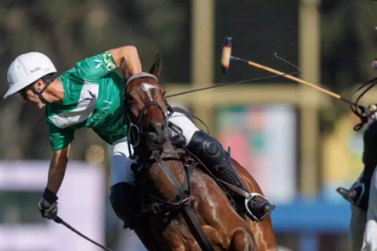 Un jugador de polo con camiseta verde y casco blanco montando un caballo marrón en plena acción durante un partido.