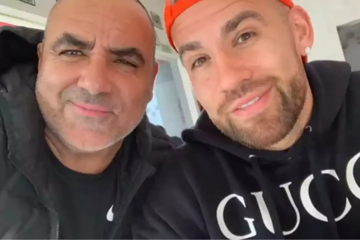 Two men pose together for a selfie, one wearing an orange cap and a black sweatjersey with the word Gucci, the other wearing a black jacket. Two men pose together for a selfie, one wearing an orange cap and a black sweatjersey with the word Gucci, the other wearing a black jacket.