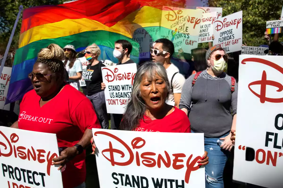 Personas en una protesta sostienen carteles con mensajes de apoyo a la comunidad LGBTQ+ y una bandera arcoíris ondea en el fondo. Personas en una protesta sostienen carteles con mensajes de apoyo a la comunidad LGBTQ+ y una bandera arcoíris ondea en el fondo.