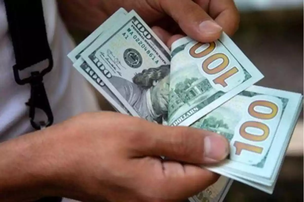 Person counting one hundred dollar bills with both hands Person counting one hundred dollar bills with both hands