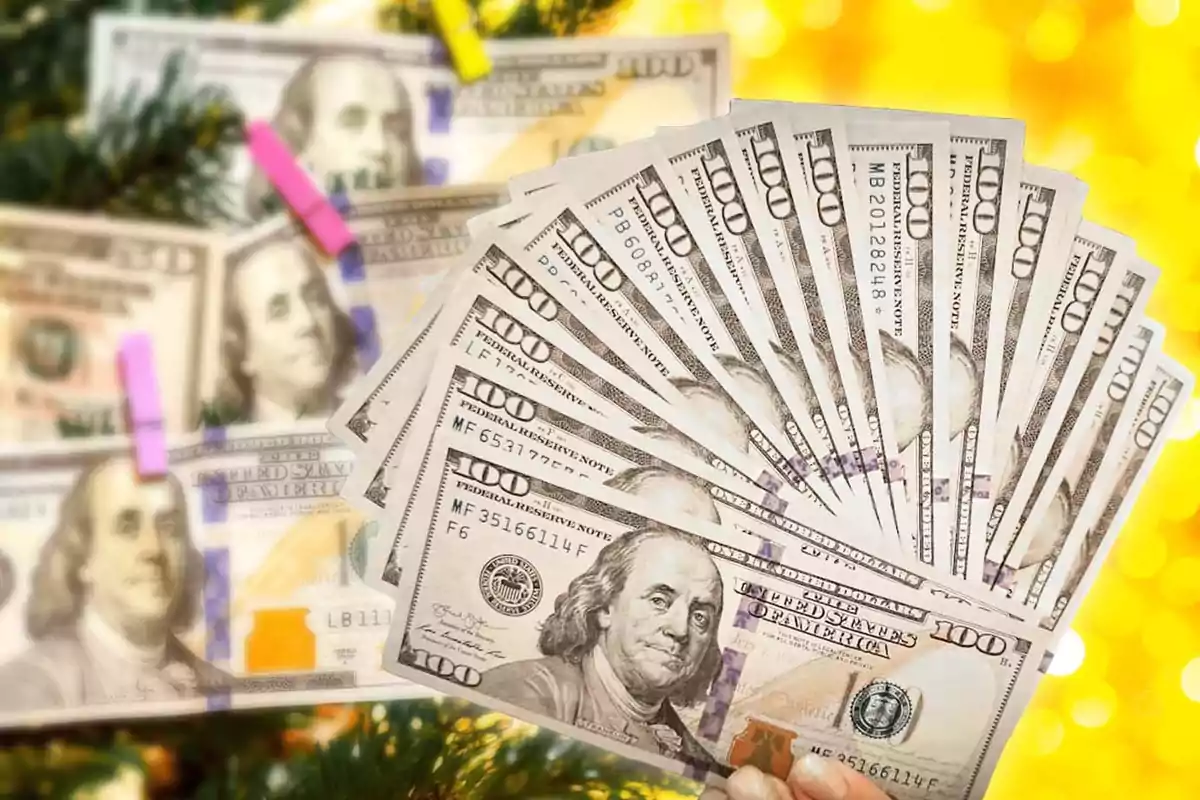 Un abanico de billetes de cien dólares frente a un fondo amarillo brillante con un arbol de Navidad decorado con billetes, representando a cuánto cerró el dólar el 25 de diciembre 2024 en Argentina.