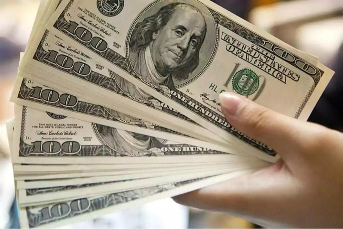 Una mano sosteniendo varios billetes de cien dólares estadounidenses.