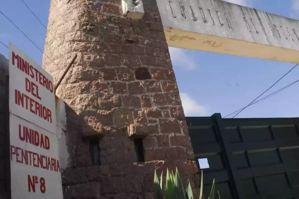Entrance of a prison with a sign that reads Ministry of the Interior Penitentiary Unit No. 8 next to a stone structure and a metal gate. Entrance of a prison with a sign that reads Ministry of the Interior Penitentiary Unit No. 8 next to a stone structure and a metal gate.