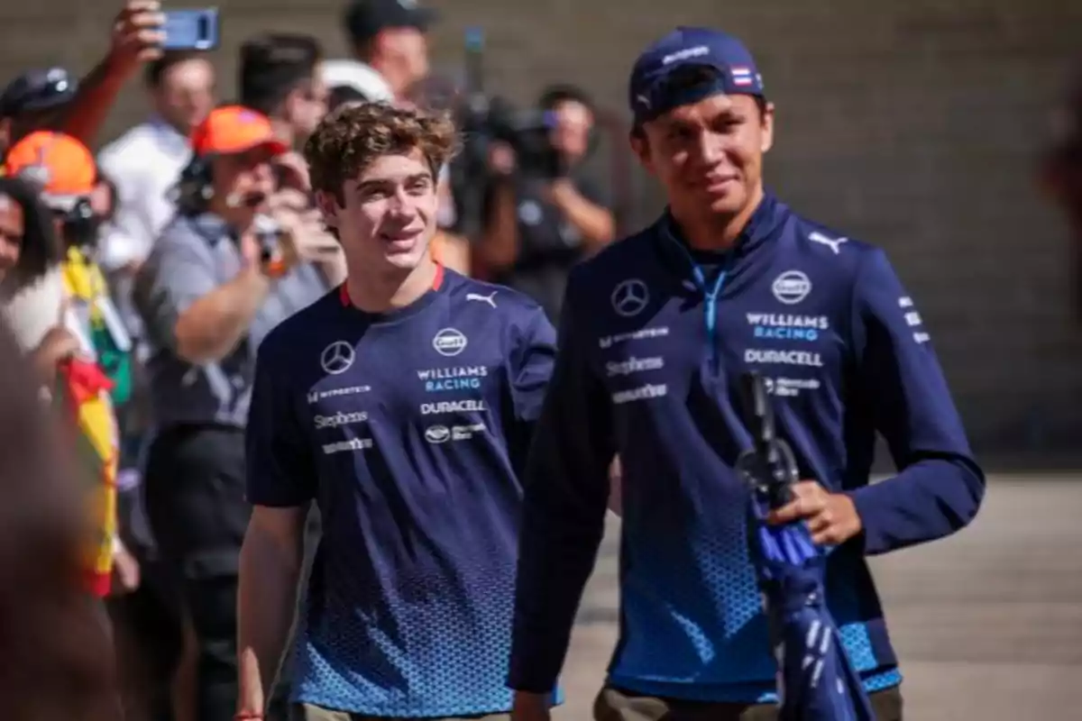 Dos personas con uniformes de Williams Racing sonríen mientras caminan en un evento al aire libre.