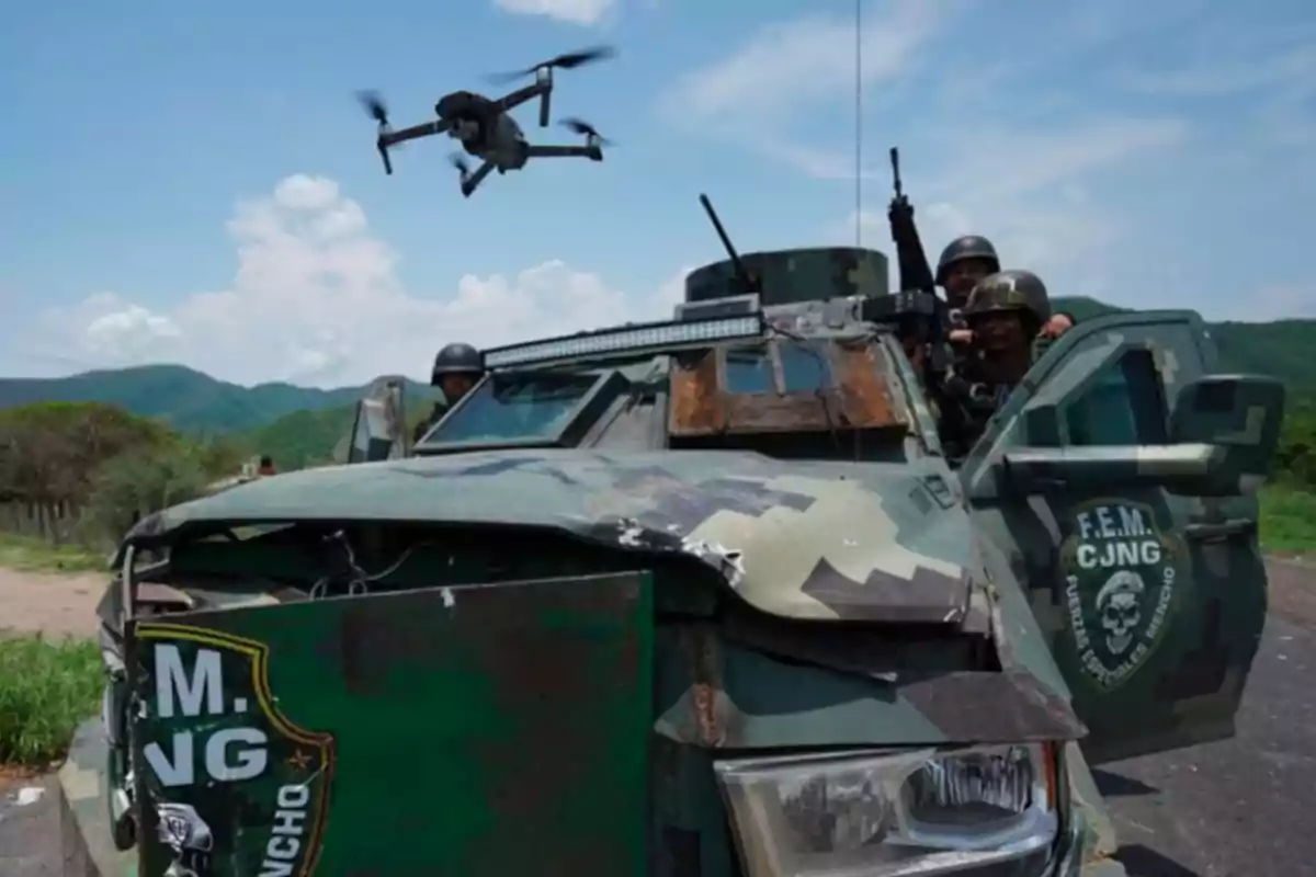 Un vehículo blindado con camuflaje verde y soldados armados, mientras un dron vuela sobre ellos en un entorno rural con montañas al fondo.