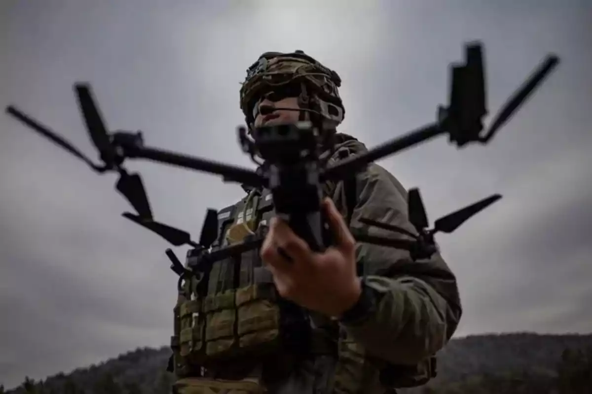 Un soldado sosteniendo un dron en un entorno al aire libre con cielo nublado.