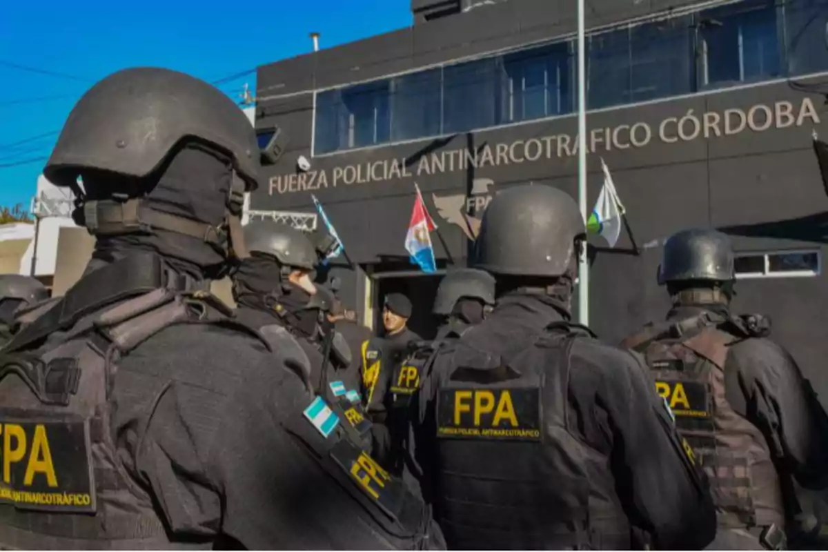 Un grupo de agentes de la Fuerza Policial Antinarcotráfico de Córdoba, vestidos con uniformes tácticos y cascos, se encuentra frente a un edificio oficial con banderas.