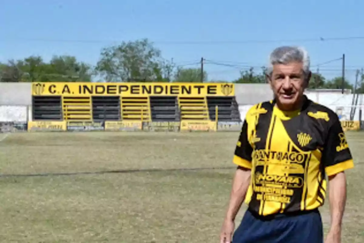 A man in a yellow and black jersey is standing on a soccer field in front of a stand that says A man in a yellow and black jersey is standing on a soccer field in front of a stand that says