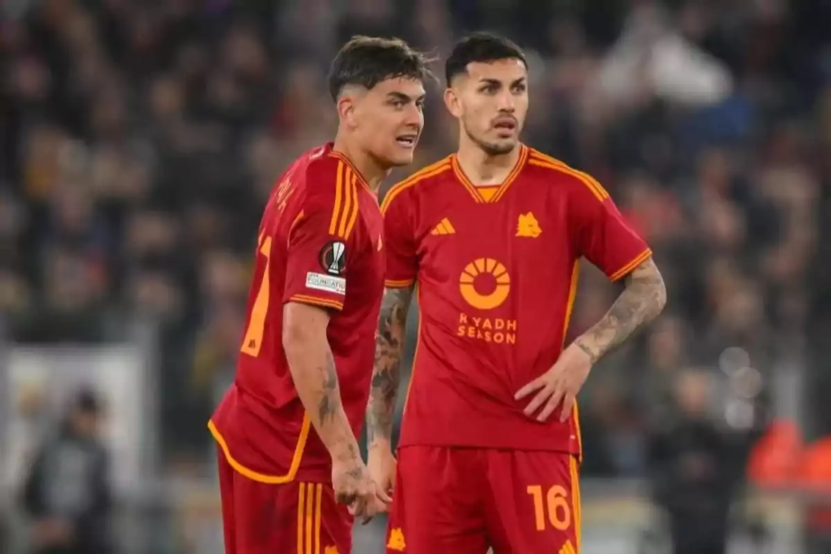 Two players in red uniforms with yellow details talk on the field during a match. Two players in red uniforms with yellow details talk on the field during a match.