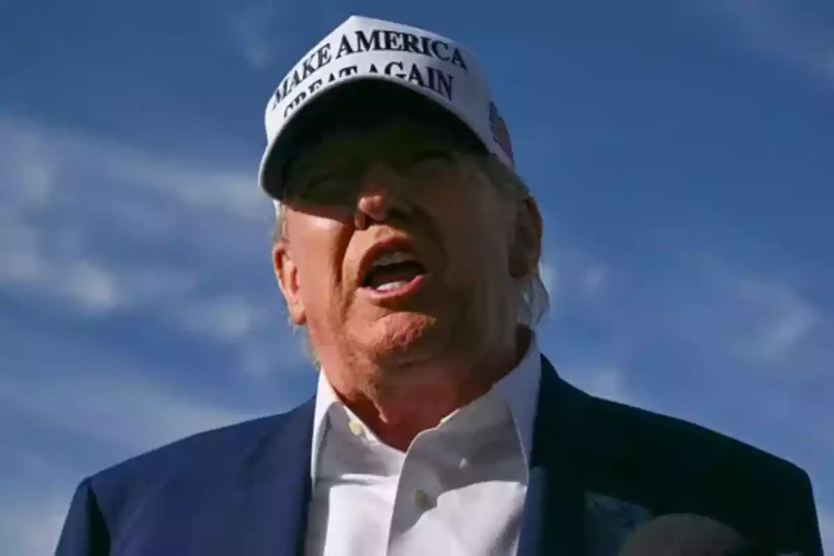 Man with a white cap that has a message in black letters and a blue sky background