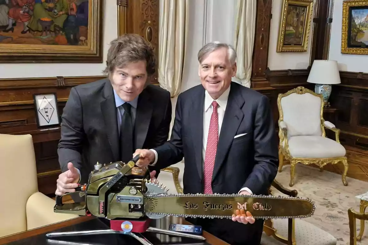 Dos hombres con traje posan sonrientes en una oficina elegante mientras sostienen una motosierra dorada que tiene la inscripción Los Fuerzas del Cielo Dos hombres con traje posan sonrientes en una oficina elegante mientras sostienen una motosierra dorada que tiene la inscripción Los Fuerzas del Cielo