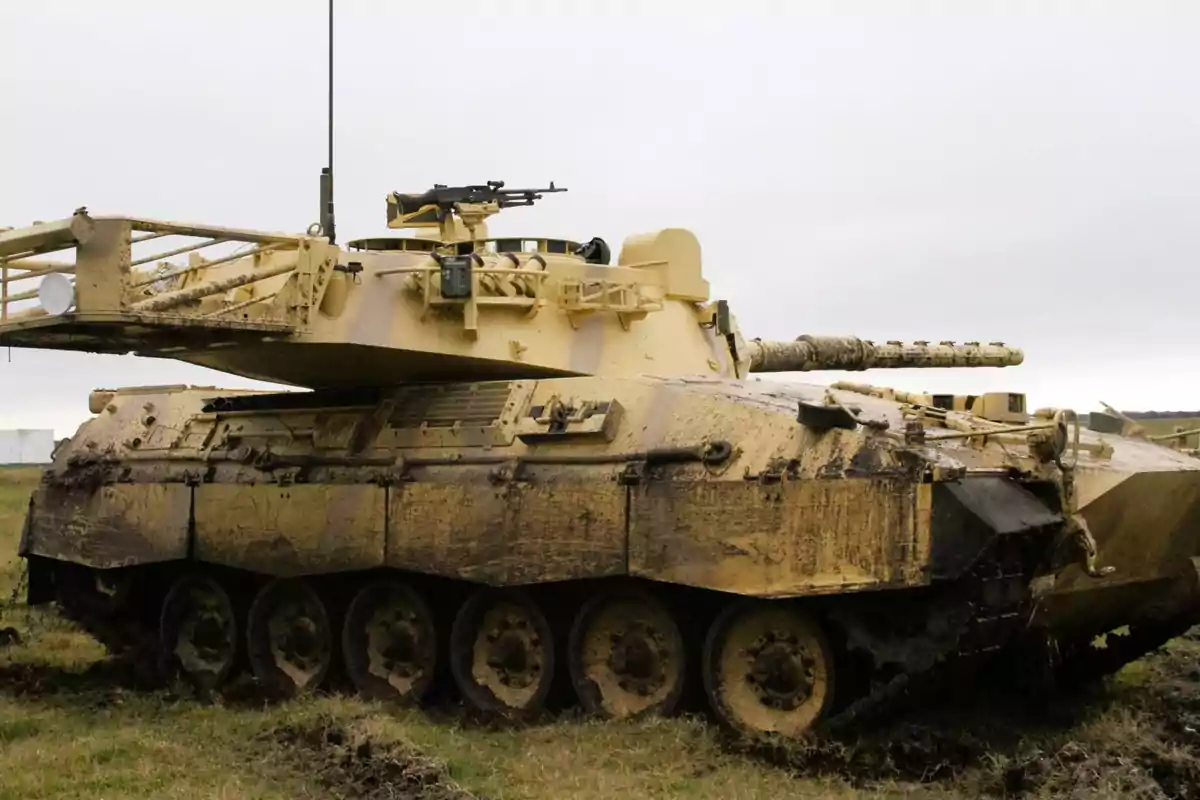 Un tanque militar de color arena con barro en sus orugas y carrocería estacionado en un campo.