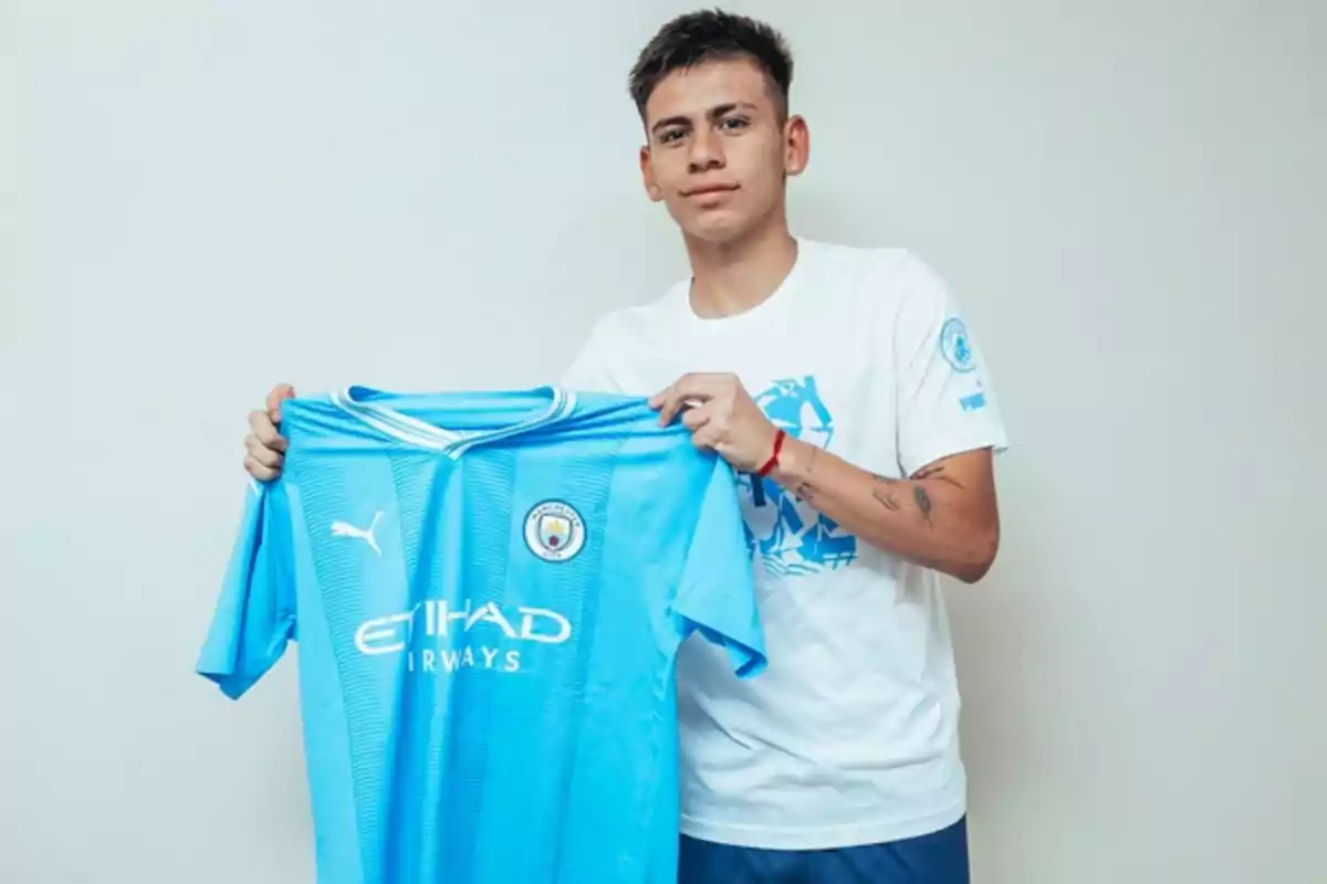 Un joven sosteniendo una camiseta de fútbol del Manchester City.