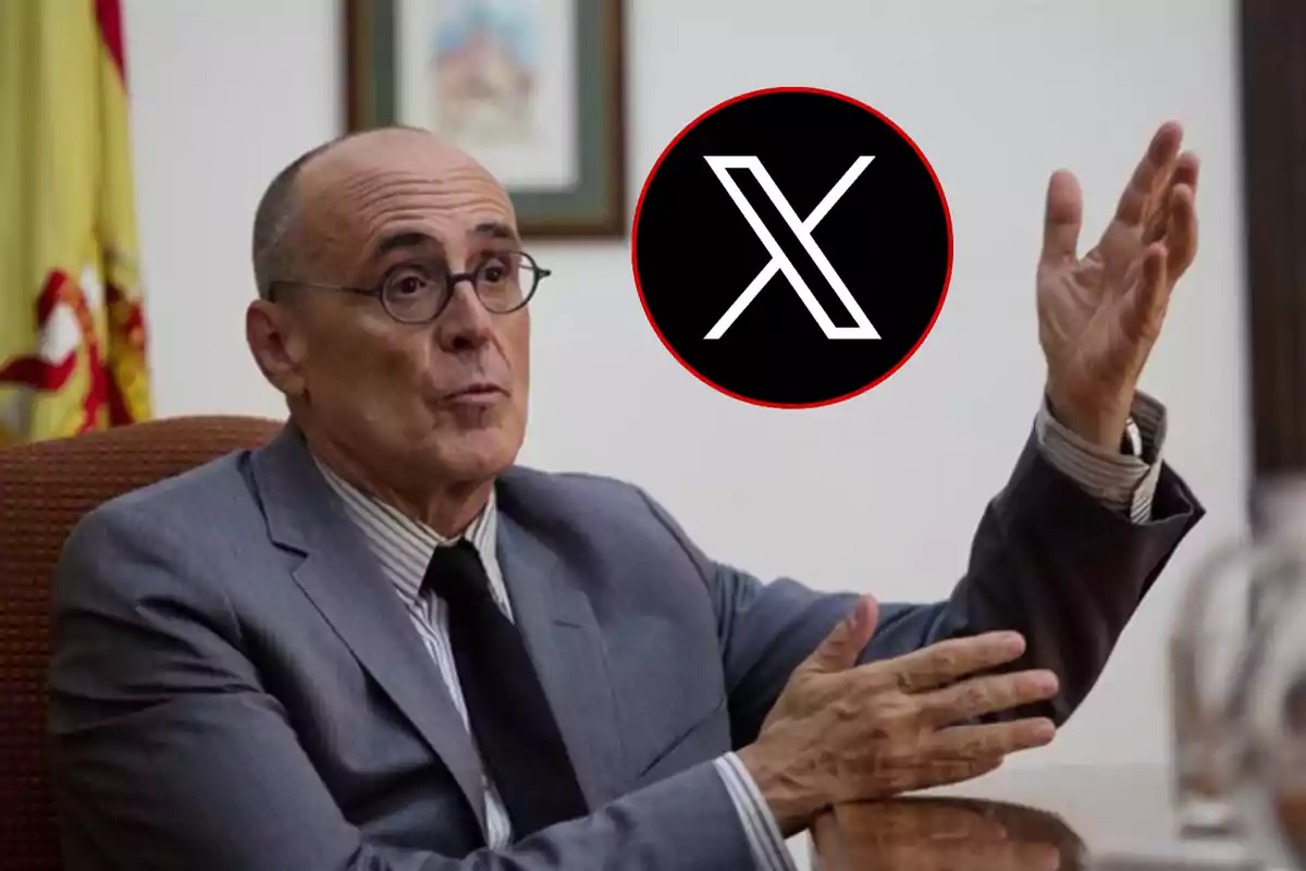 Un hombre con gafas y traje gris gesticulando con las manos, con un logotipo de una "X" en un círculo negro con borde rojo en la esquina superior derecha.