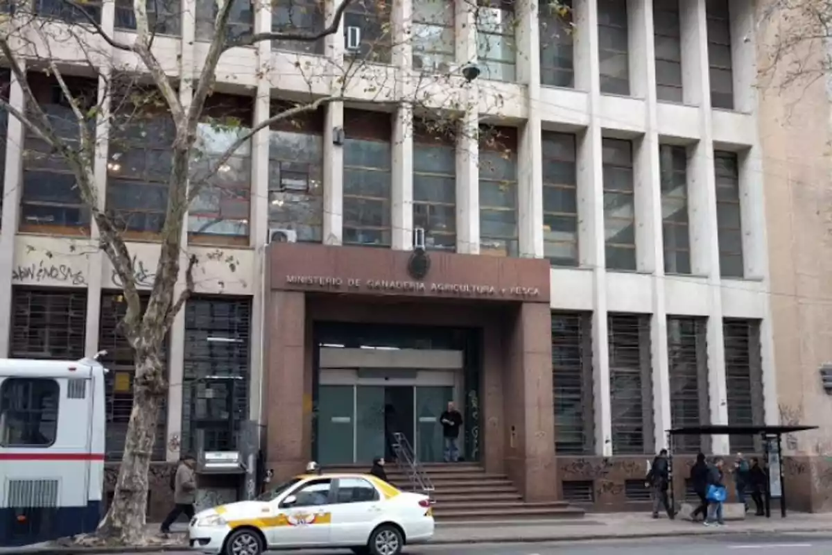 Facade of a government building with a parked taxi and people walking on the sidewalk