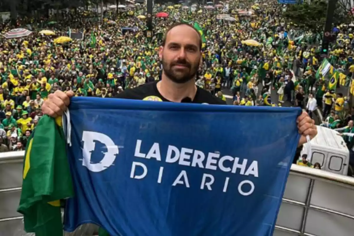 Un hombre sostiene una bandera azul con el texto "LA DERECHA DIARIO" frente a una multitud de personas vestidas de verde y amarillo.