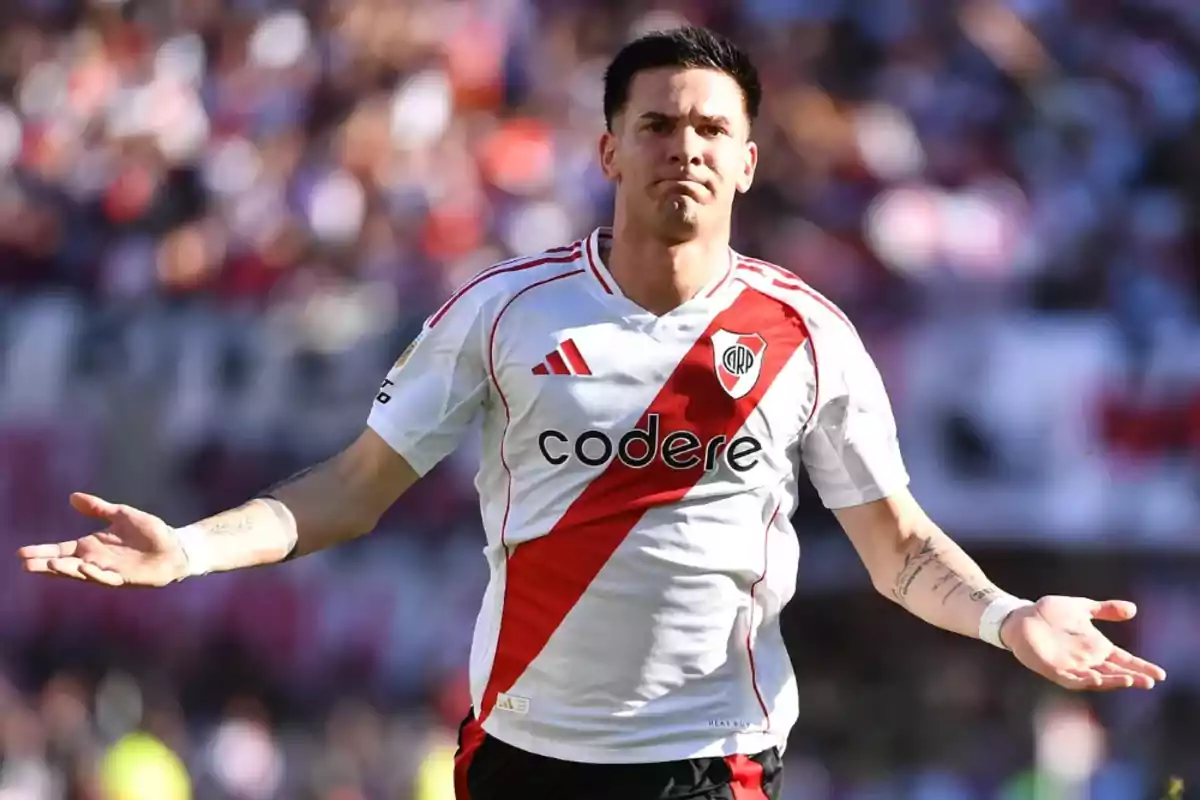 Un jugador de fútbol con el uniforme de River Plate extiende los brazos en un gesto de confusión o pregunta durante un partido. Un jugador de fútbol con el uniforme de River Plate extiende los brazos en un gesto de confusión o pregunta durante un partido.