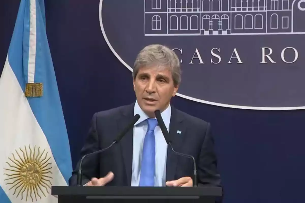 A man in a suit and blue tie speaks at a podium with two microphones in front of an Argentine flag and a background that says "Casa Rosada."