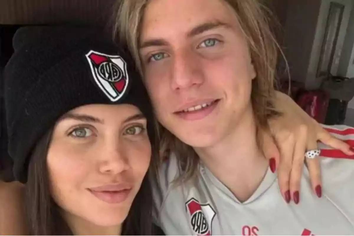 Two people pose together, one wearing a cap and the other a t-jersey, both with a soccer team's crest.
